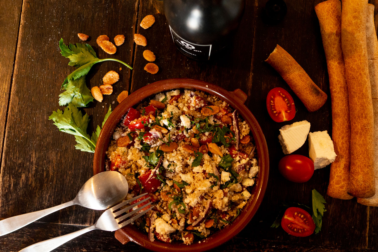 Salat mit Tomaten, Kräutern und Käse in einer Tonschale, daneben Brotstangen und eine ART-OF-OIL-Flasche